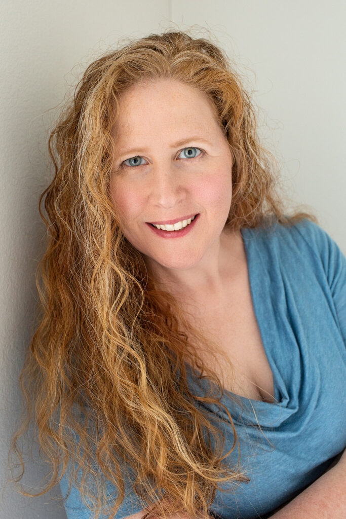 self portrait of Jennifer leaning against wall. Long red hair and blue top.