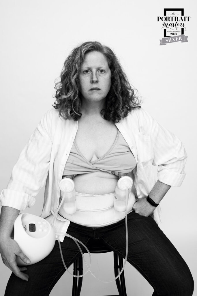 Photographer's self-portrait. Woman is using breast pump and is seated, facing the camera.